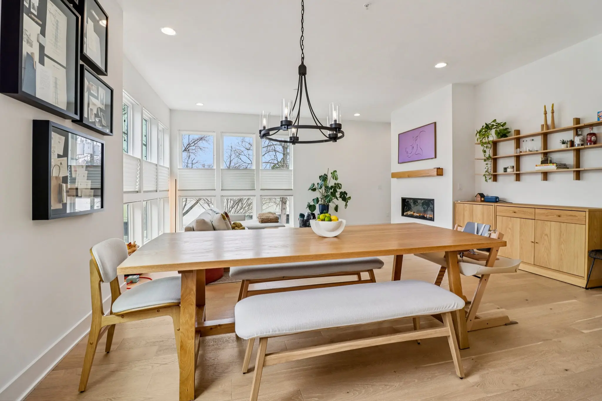 Dining area with an oak trestle table and bench beneath a black iron chandelier.