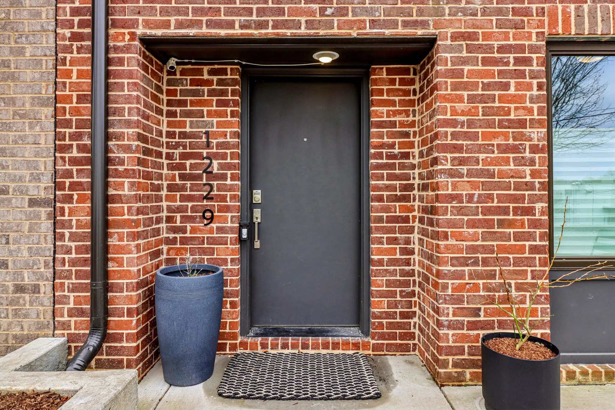 Recessed brick entry with a dark door, black hardware and vertical 1229 house numbers.