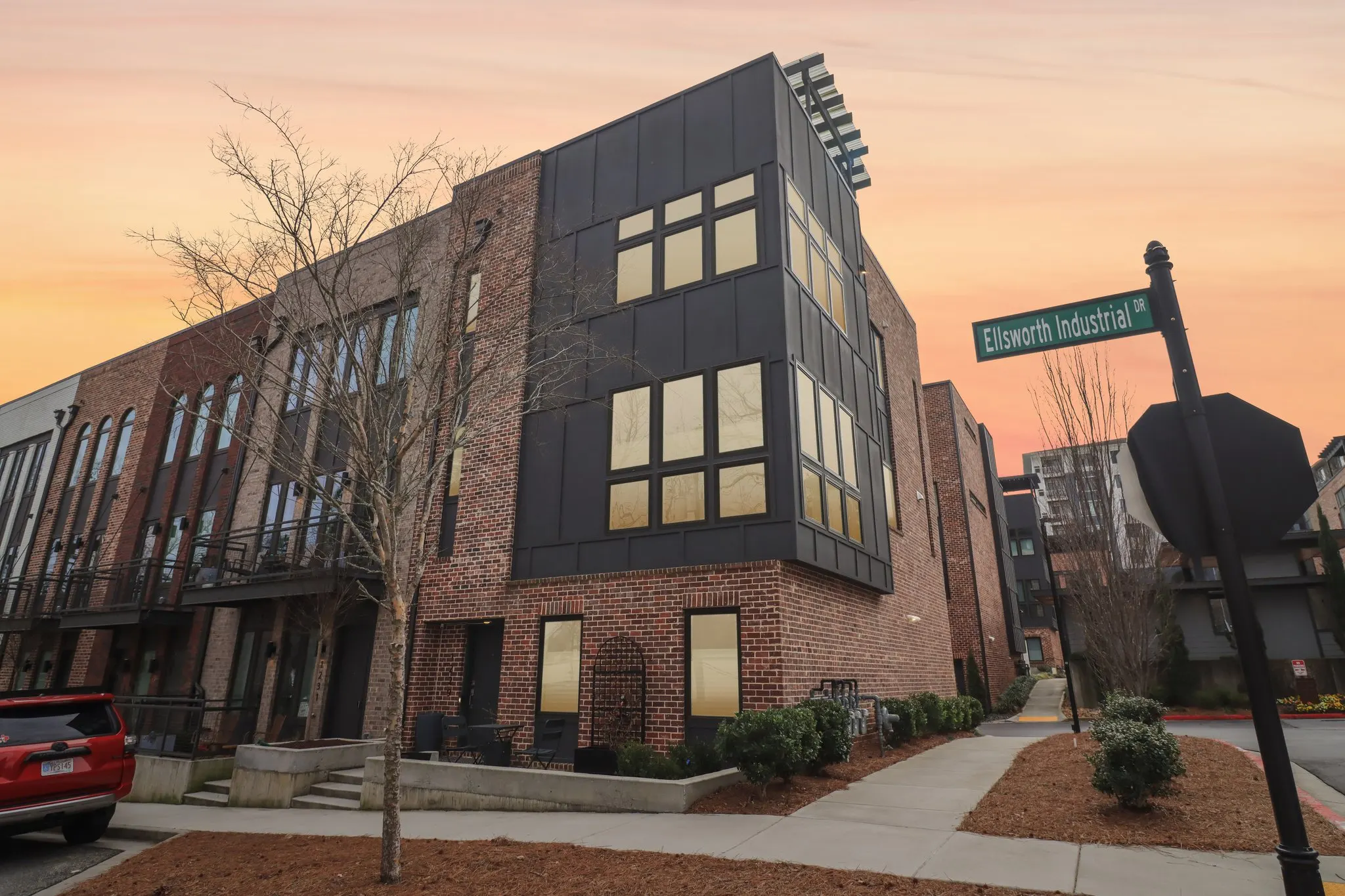 1229 Chelsea Cir NW at twilight — the red brick end unit with black steel-framed window bays and warmly lit interiors.