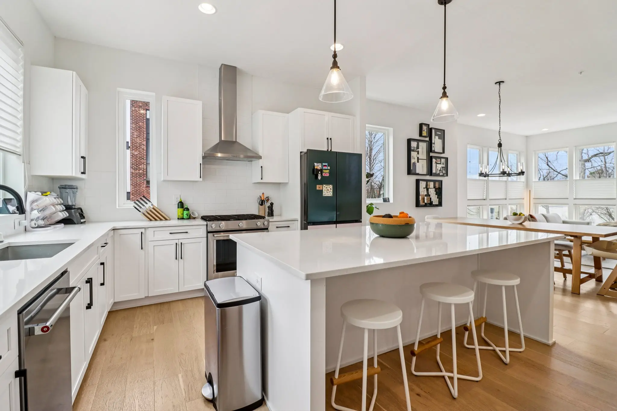 Chef’s kitchen with a professional stainless gas range, vent hood, quartz island and three barstools.