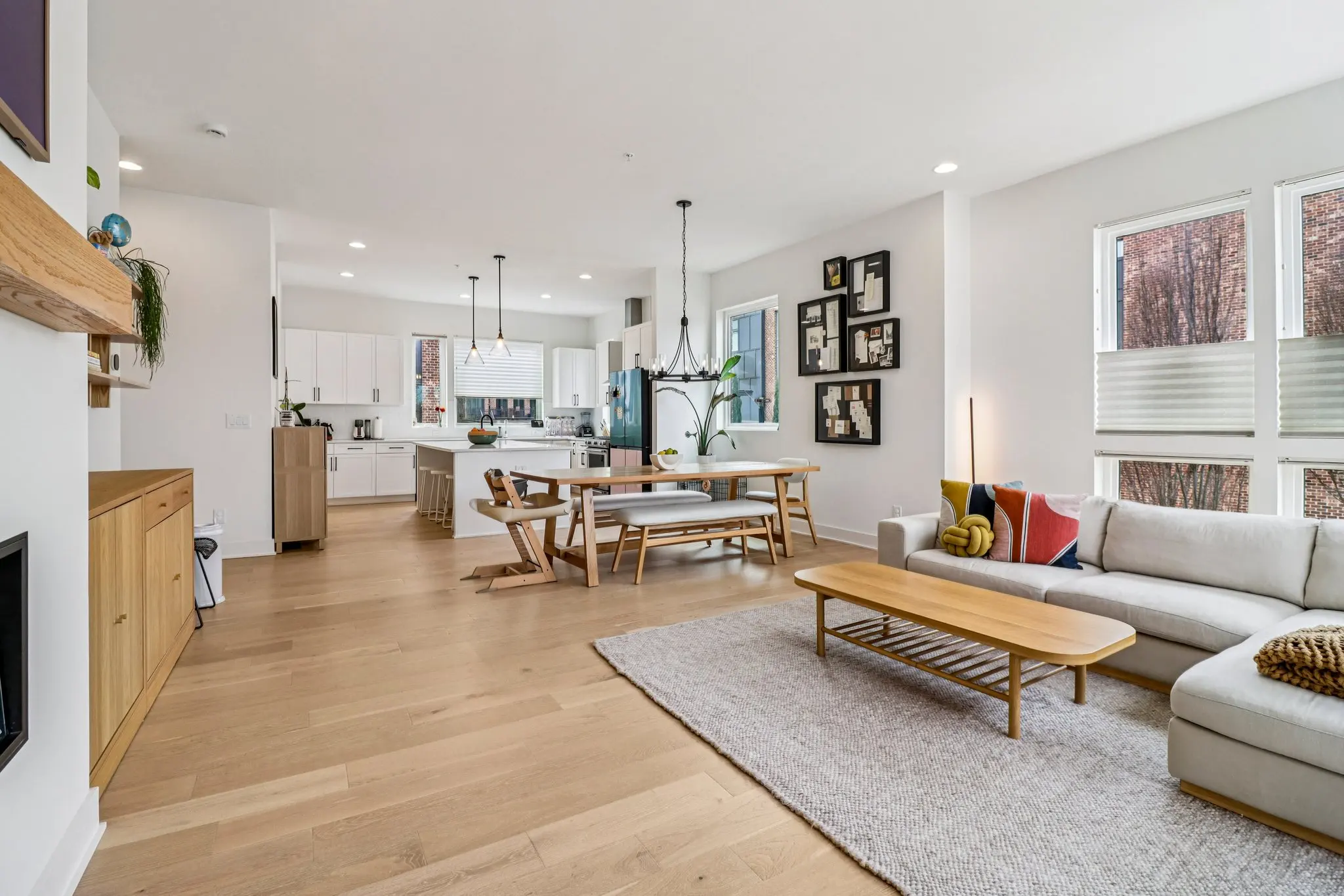 Open main level with wide-plank oak floors running from the living room through the dining area to the white kitchen.