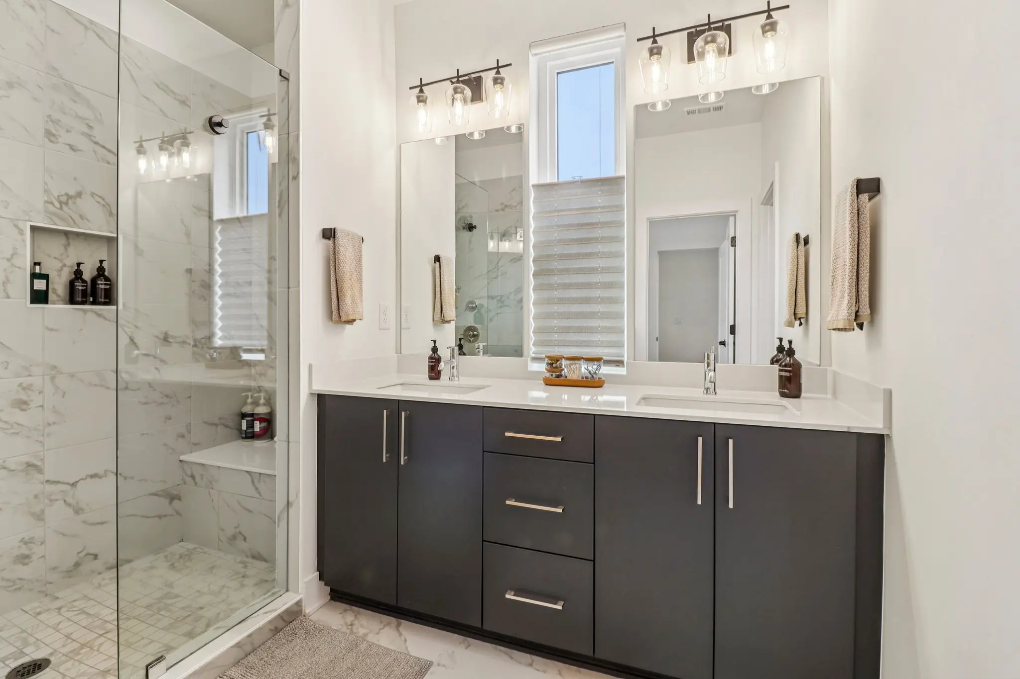 Primary bathroom double vanity in dark shaker cabinetry with quartz counter, twin mirrors and globe sconces.