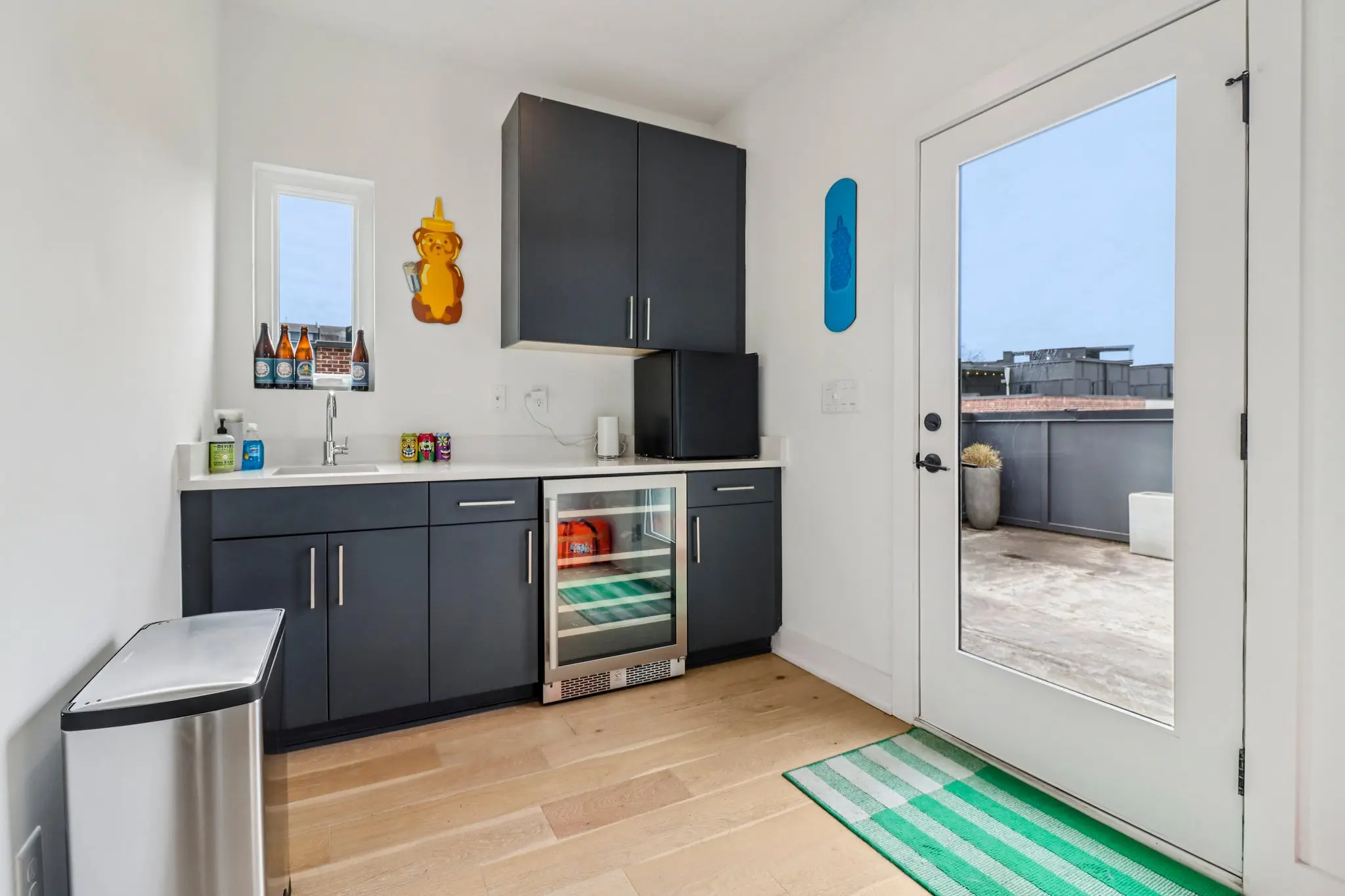 Wet bar with dark cabinets, bar sink and beverage refrigerator beside a glass door onto the rooftop terrace.