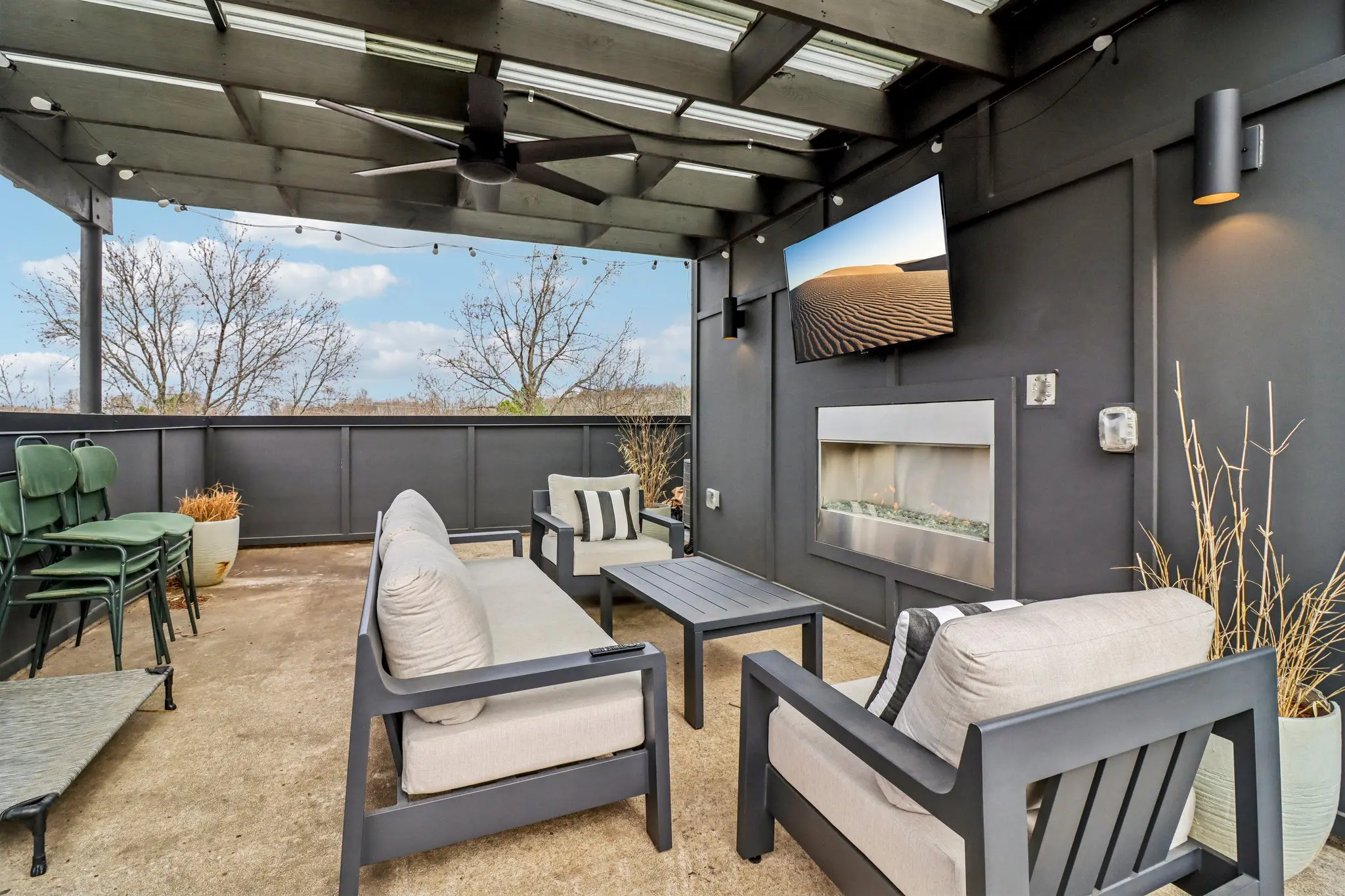 Rooftop terrace lounge seating around a coffee table facing a linear fireplace and outdoor TV under a pergola.