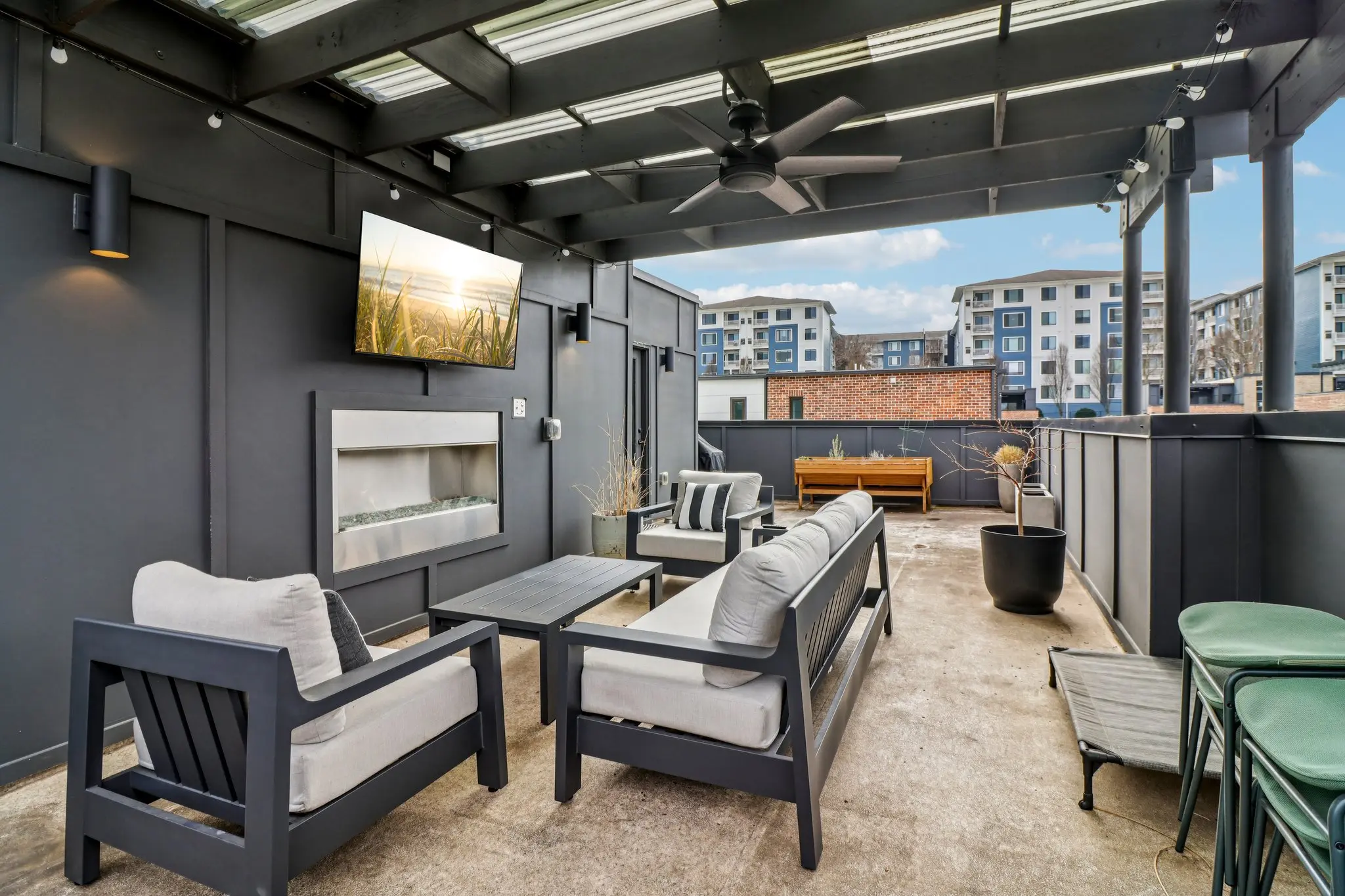 Covered rooftop terrace with a linear gas fireplace, mounted TV, ceiling fan and pergola over lounge seating.